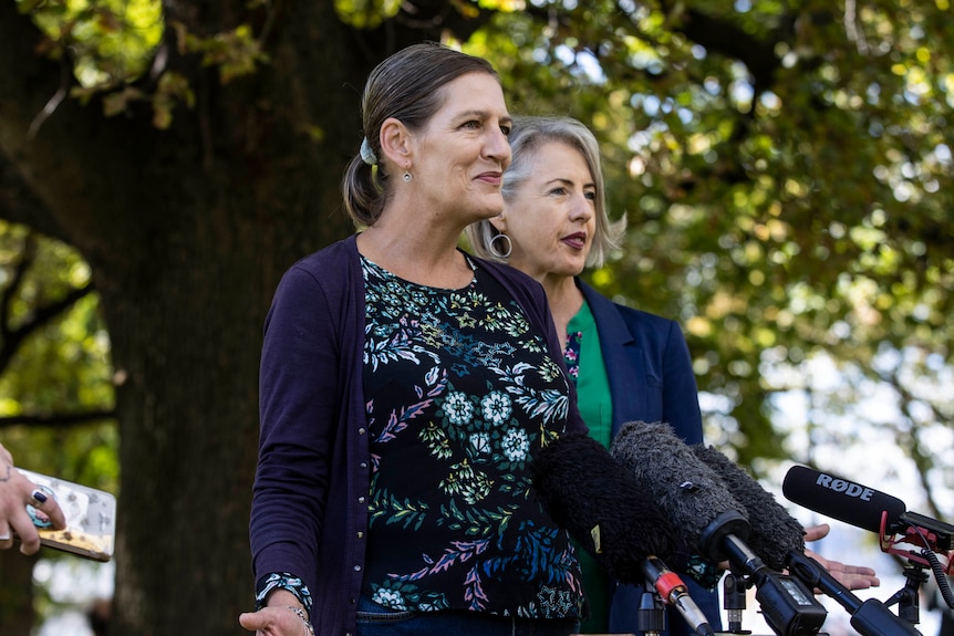 Two women stand behind a microphone at a press conference.