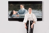 A woman stands in front of a screen which has an image of a man holding a woman in water