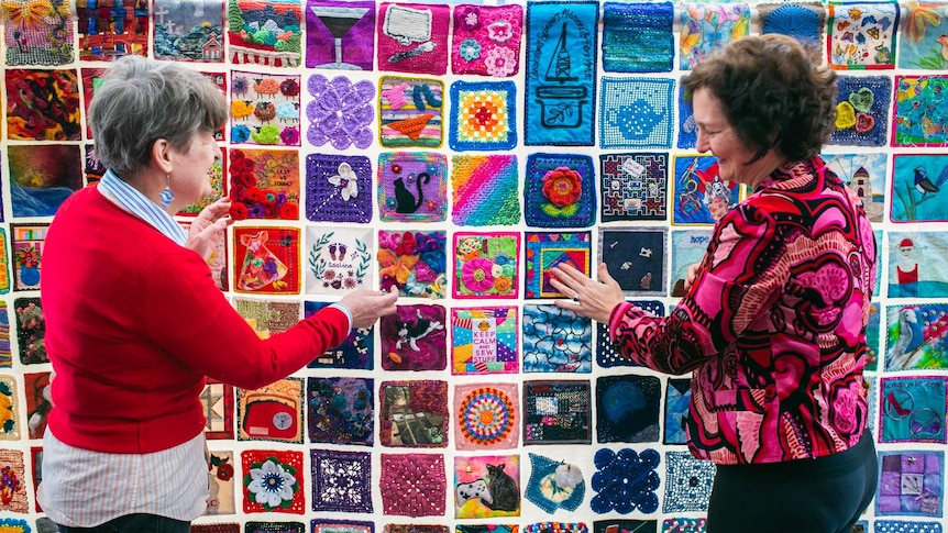 Two ladies looking closely at a quilt.