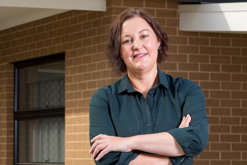 Woman stands in front of house with arms crossed