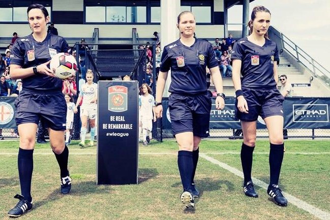 Four women dressed in referees' black uniforms stride onto the grounds ahead of a match