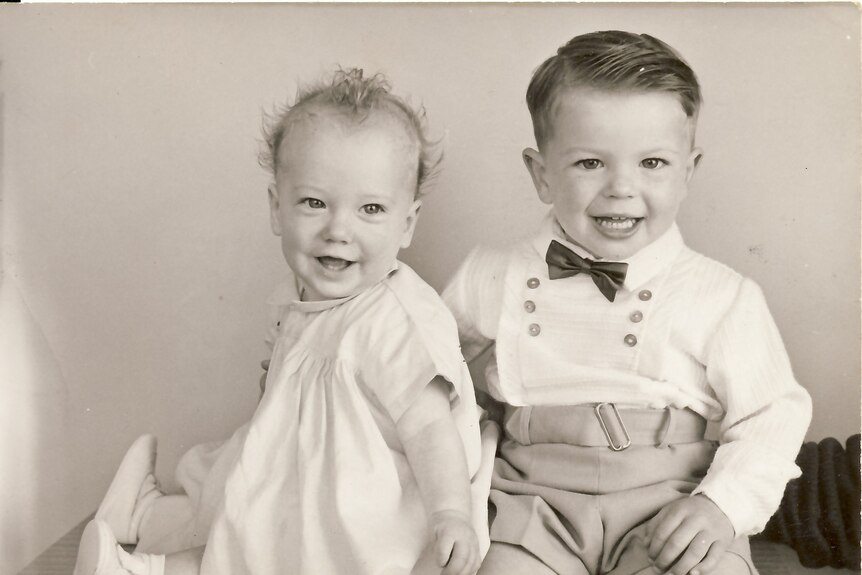 A sepia toned photo of two smiling toddlers dressed in white for a formal photograph