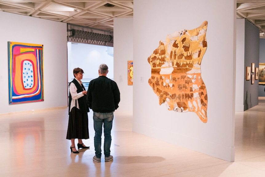 A man and a woman talk in an art gallery