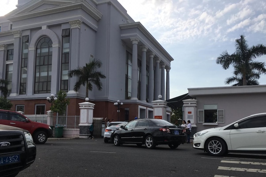 A view of a building with high arches and columns with cars driving on the road.