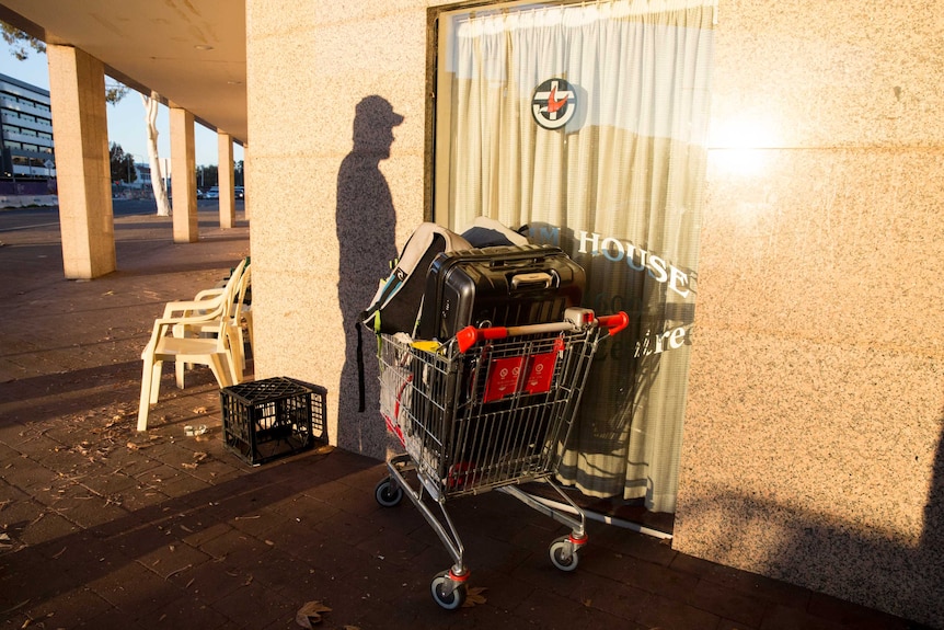 A man's shadow near his trolley of belongings.