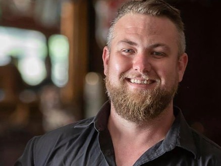 A man with a beer smiles at the camera.