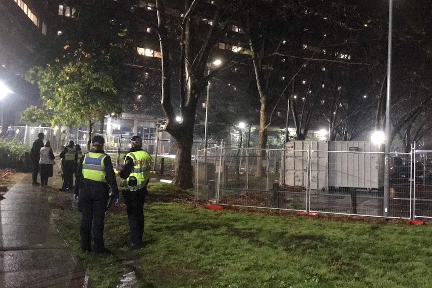 Police stand near temporary fencing at night.