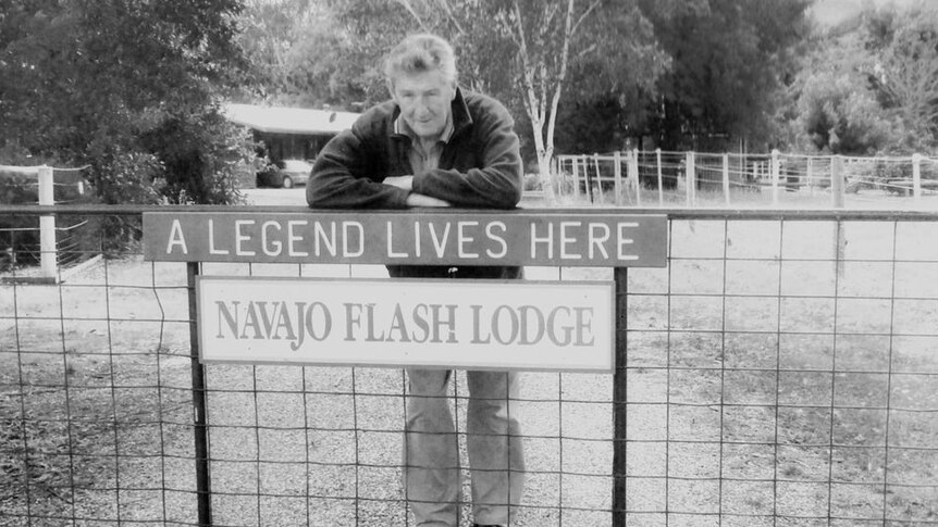 Raymond Kelly leans on his front gate where the sign "A legend lives here" hangs.