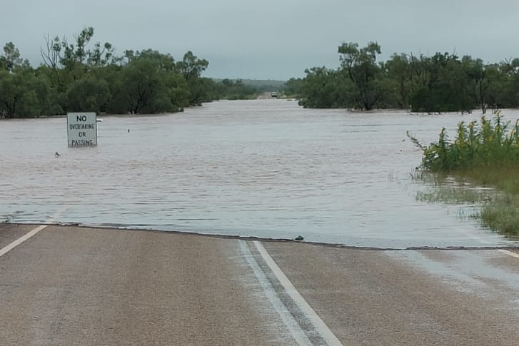 A sealed road in a remote area, with a portion covered in floodwater.
