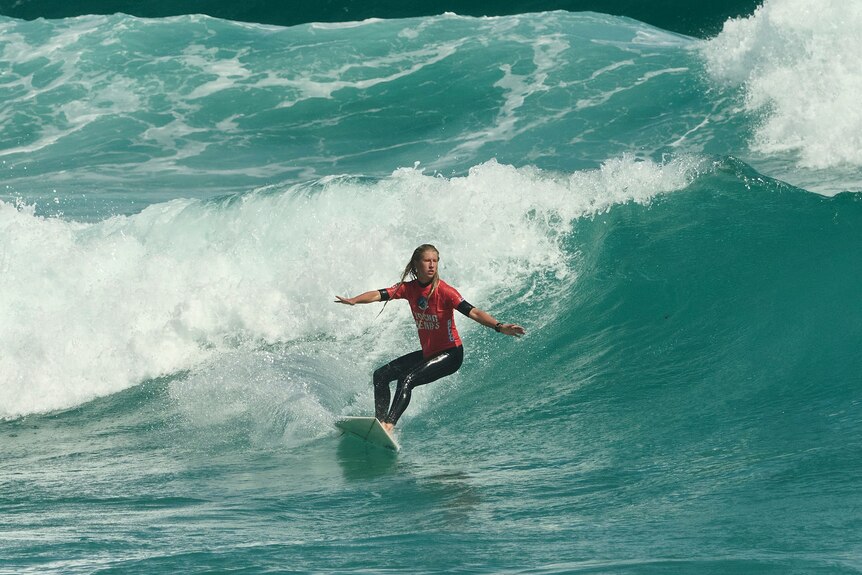 A young female surfer in a red top surfs on crashing waves