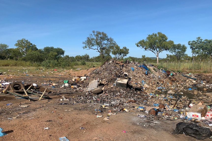 pile of rubbish on brown dirt with trees and grass in the background