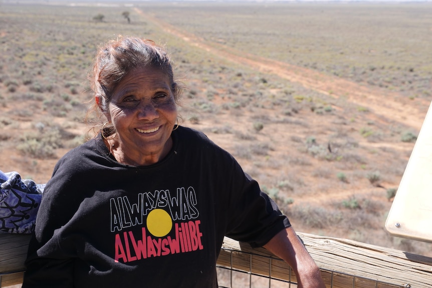 A woman, wearing a jumper that says Always Was, Always Will Be, smiling.