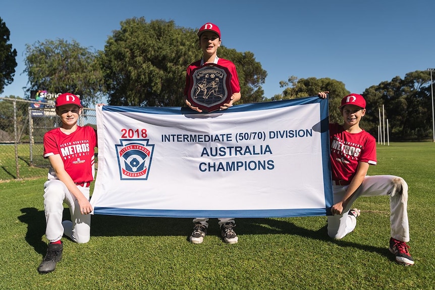 Perth Little league players hold up a banner and shield.