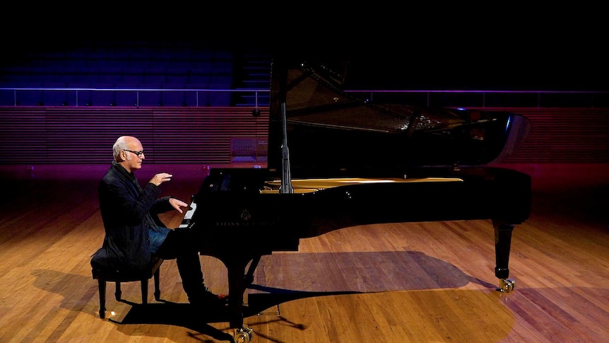 A man sits at a piano in an empty concert hall.