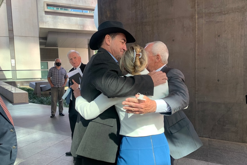 Three councillors hug outside court.