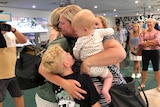 A family hug and cry in an airport.