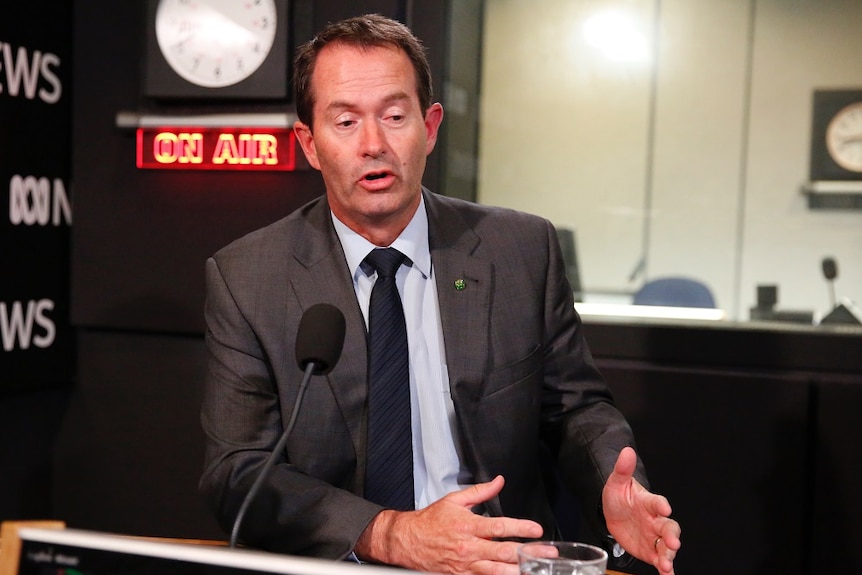 A man in a dark suit gestures during an interview in a radio studio.