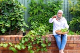 Lina Jebeile sitting on a brick wall in her garden, holding a plate of freshly picked tomatoes.