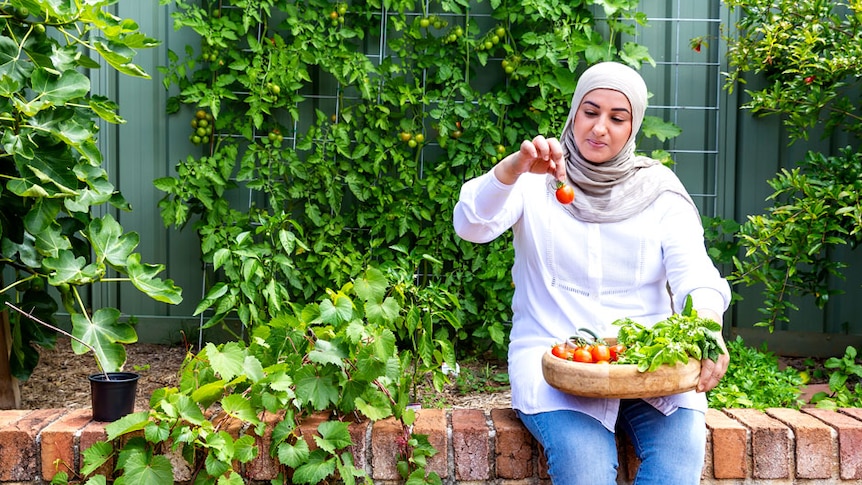 Lina Jebeile sitting on a brick wall in her garden, holding a plate of freshly picked tomatoes.