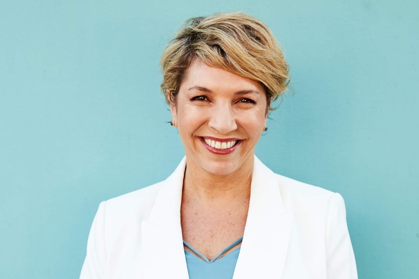 a woman in white smiling in front of a sky blue background