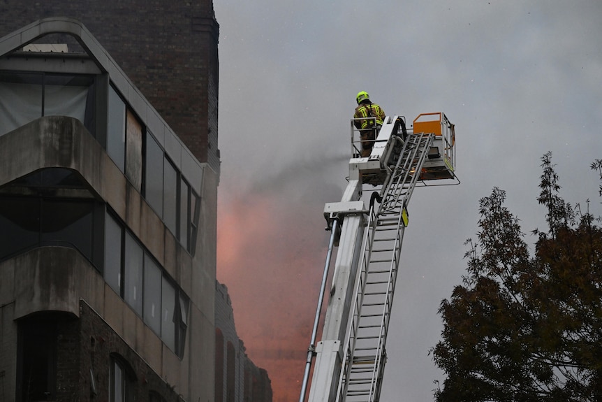 a firefighter on a crane as a blaze burns a building
