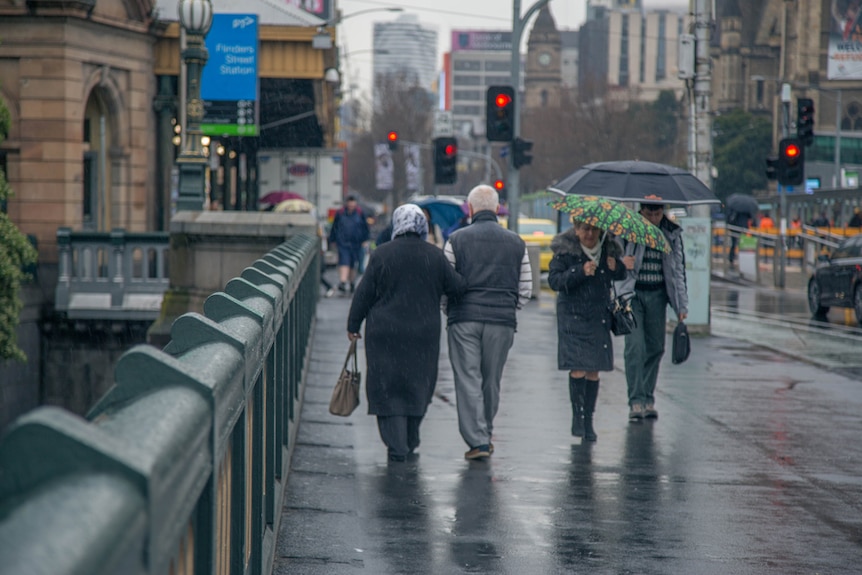 Pedestrians shelter under umbrellas as rain falls in Melbourne.