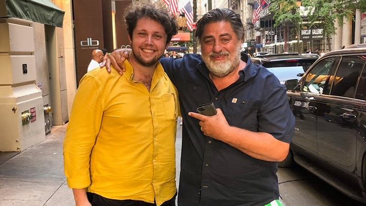 Two men smile at the camera while standing in the street in New York.