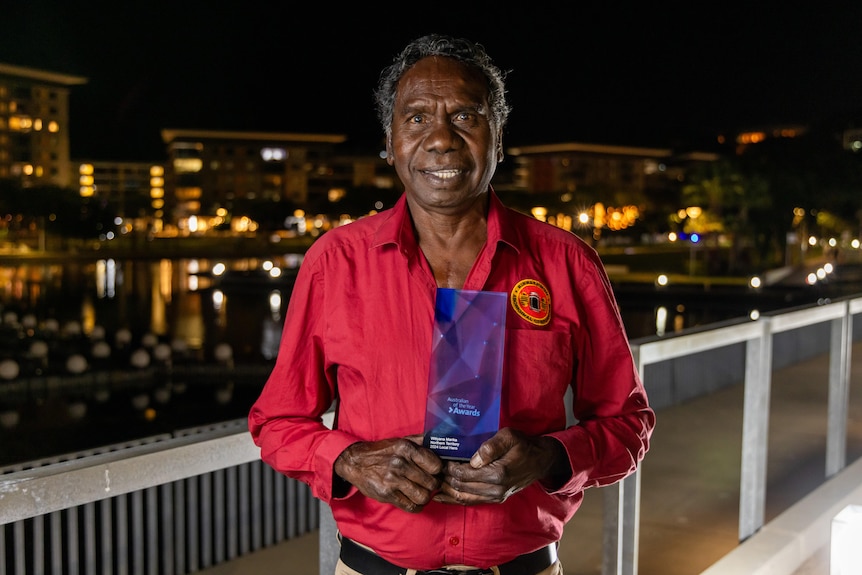 An Indigenous man holds a glass award.
