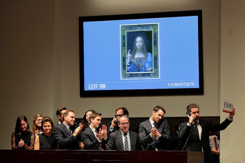 Bidders stand under a screen showing the da Vinci painting.
