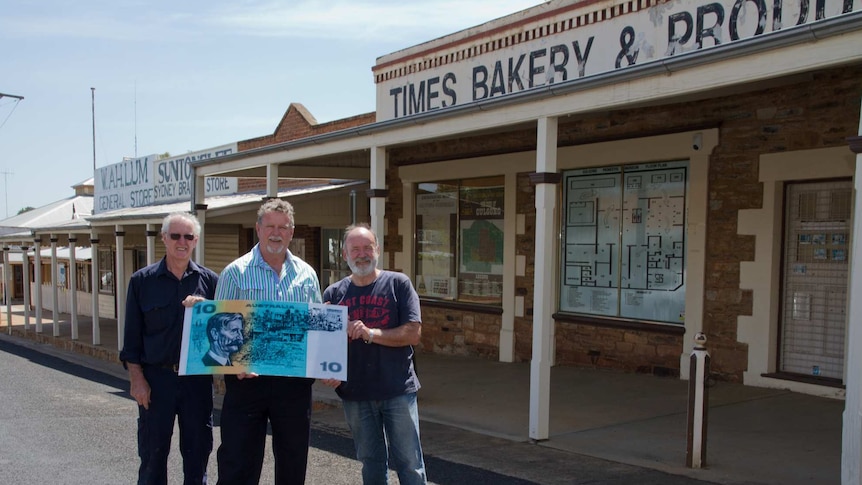 three men holding a large $10 note stand in front of the Times Bakery in Gulgong, which was featured on the note.