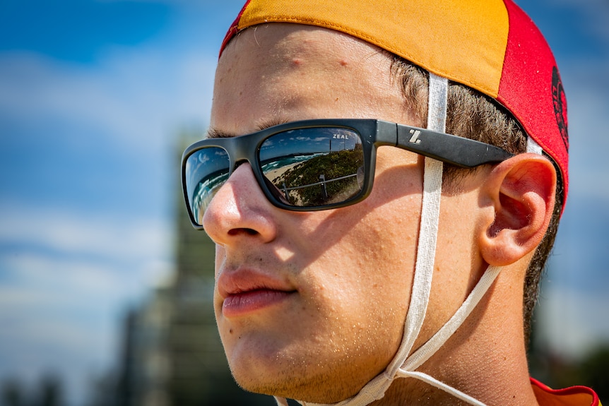 An extreme close-up of Spyros looking into the distance, the beach reflected in his dark sunglasses.