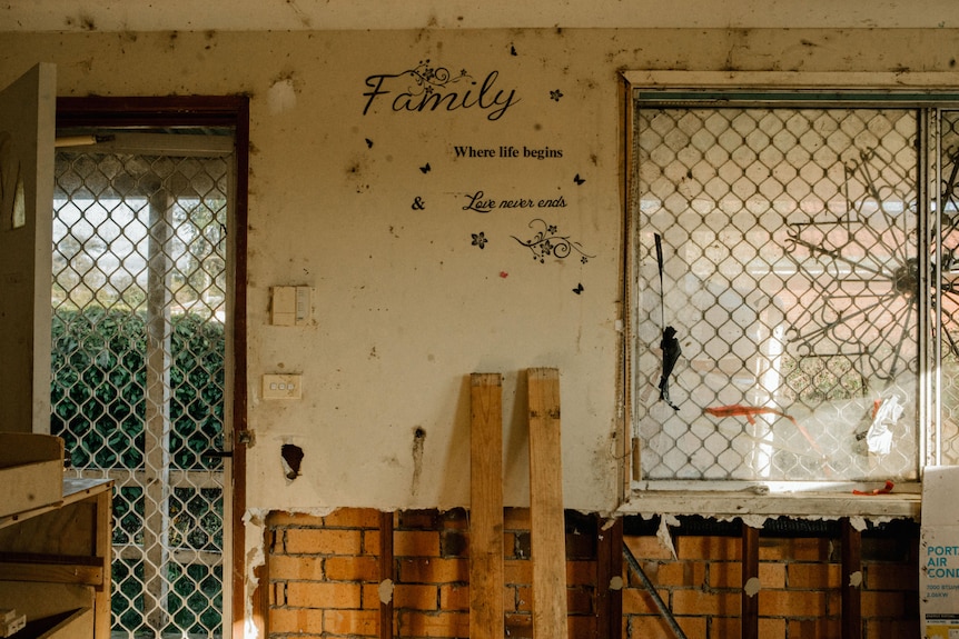 A wall with large sections of plasterboard ripped away. A sticker on the wall says 'Family where life begins love never ends'