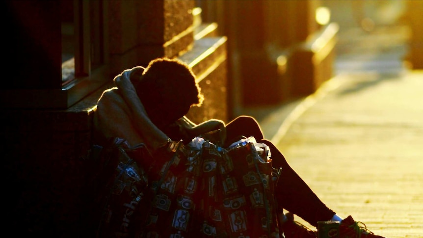 A homeless man on a street huddling into a blanket