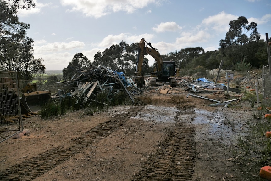 Digger sitting beside the timber and mortar remains of demolished new home