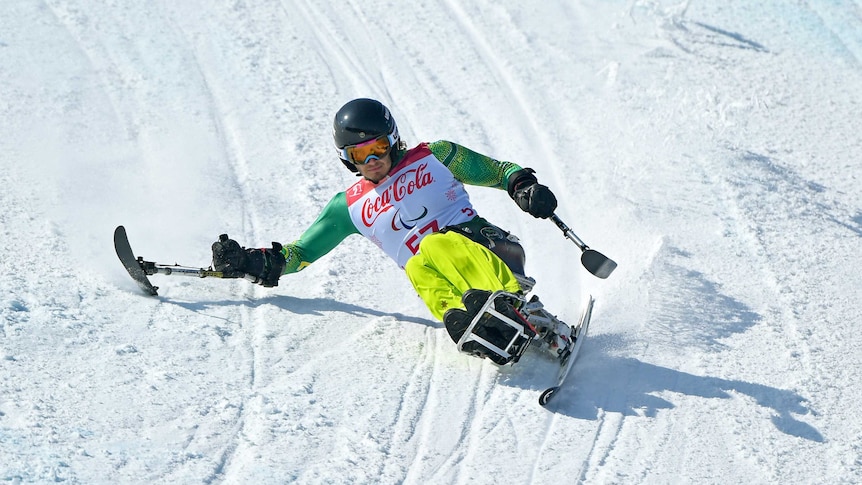 Sam Tait reaches out with his right ski pole during a seated ski downhill run.