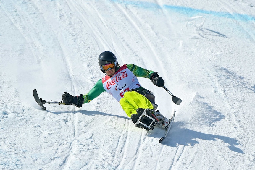 Sam Tait reaches out with his right ski pole during a seated ski downhill run.