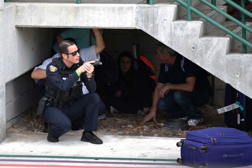 A Florida policeman holds his gun and shields hiding civilians during a shooting an a Fort Lauderdale airport.