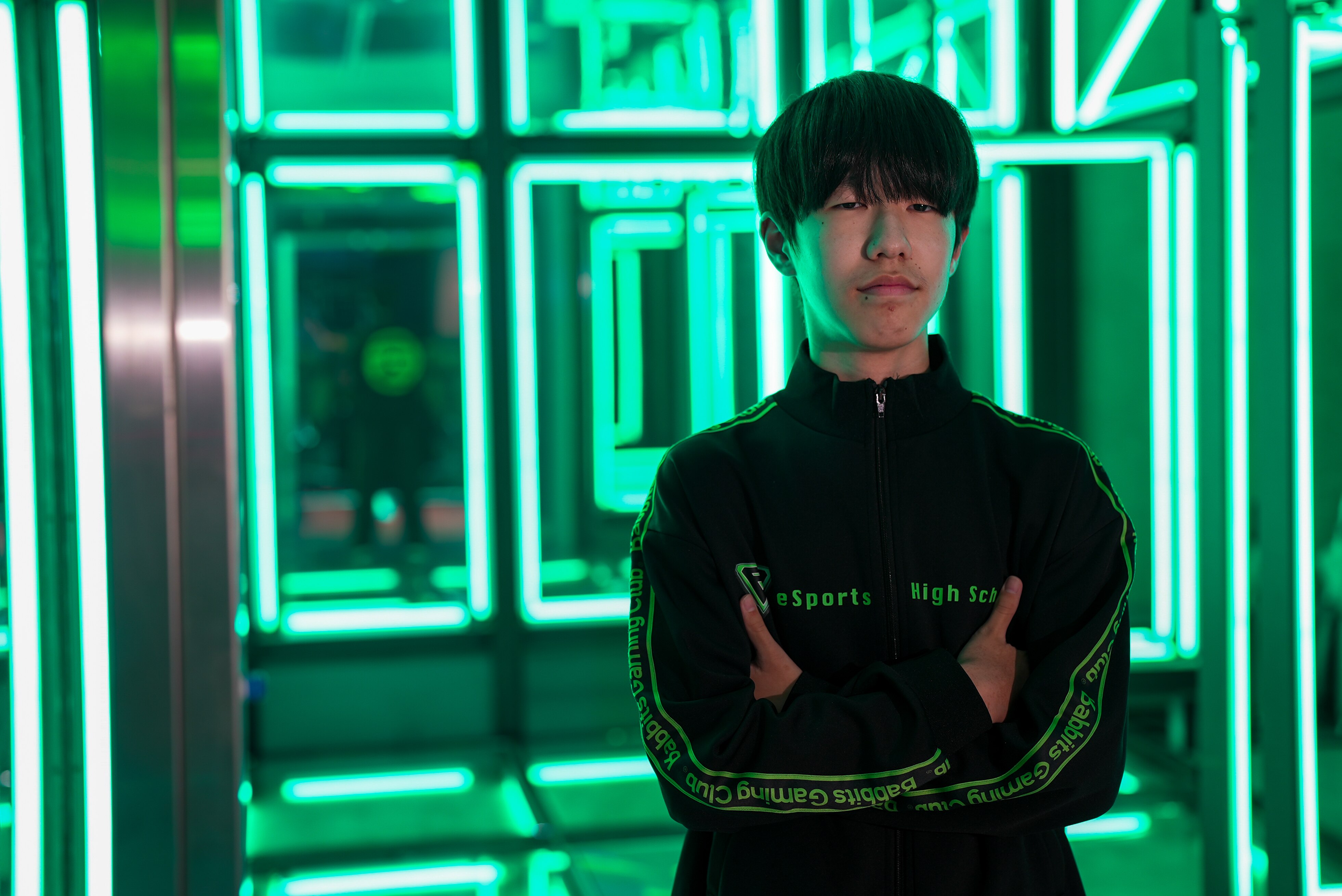 Um adolescente japonês está com os braços cruzados em uma sala.