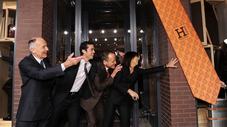 A group of people gesturing at a giant swinging orange tie 