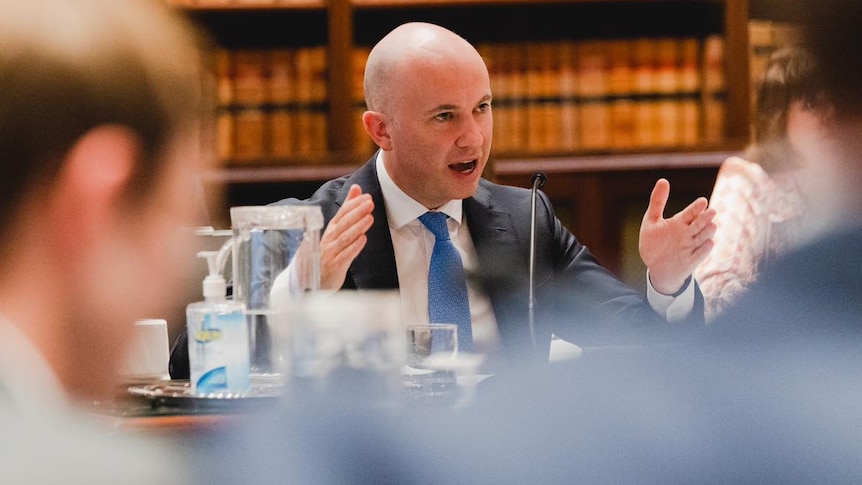 a man sitting at a table talking and moving his hands