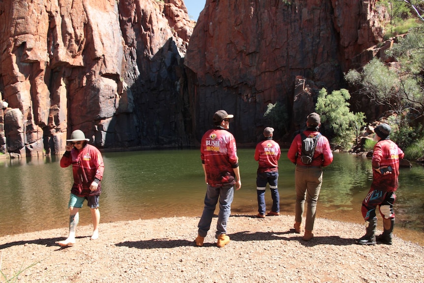 Men, wearing jeans and pink shirts, stand on the edge of a large rock pool called Python Pool