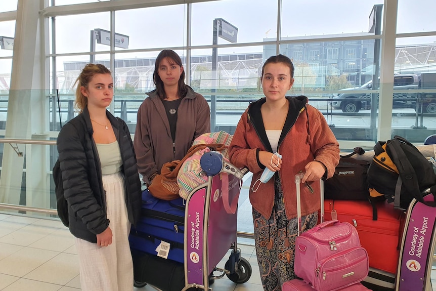 three women looking glum with luggages at the airport