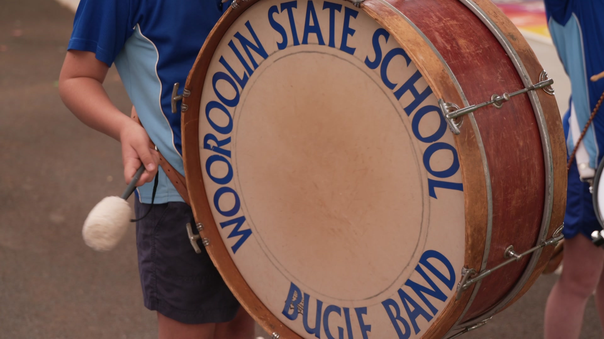 Bass drum with 'Wooroolin State School Bugle Band' written around the perimiter. A child is playing it.