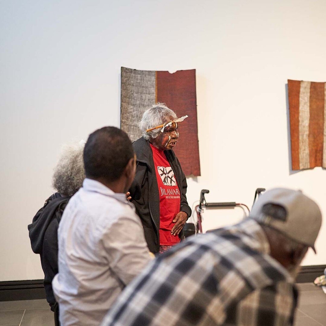 Kaye Brown stands up while giving a speech. Bark paintings can be seen on a wall in the background.