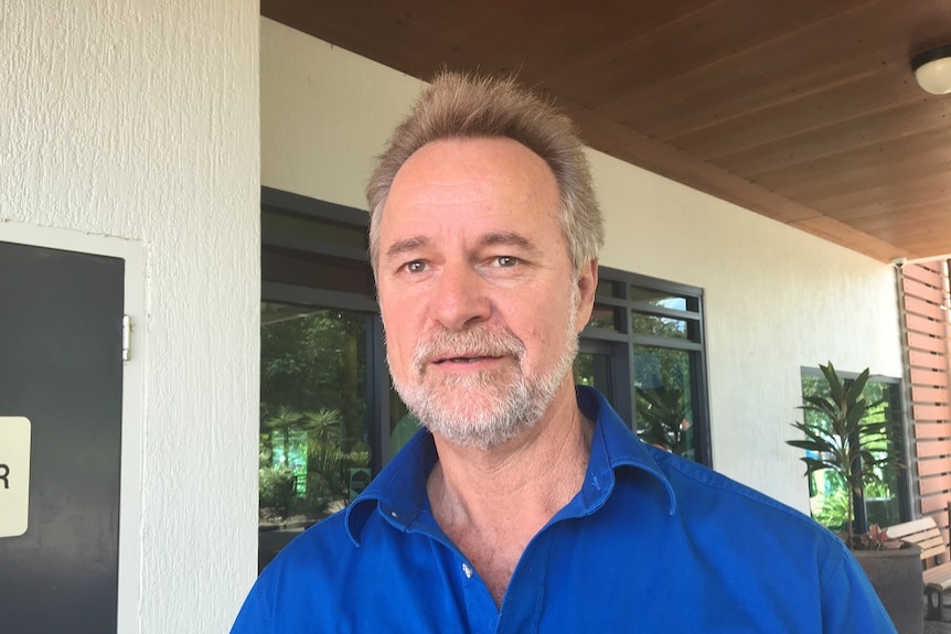 Nigel Scullion stands outside a building, smiling, wearing a blue shirt.