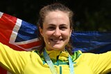 An Australian female road cyclists stands with the national flag behind her while wearing her Comm Games gold medal.