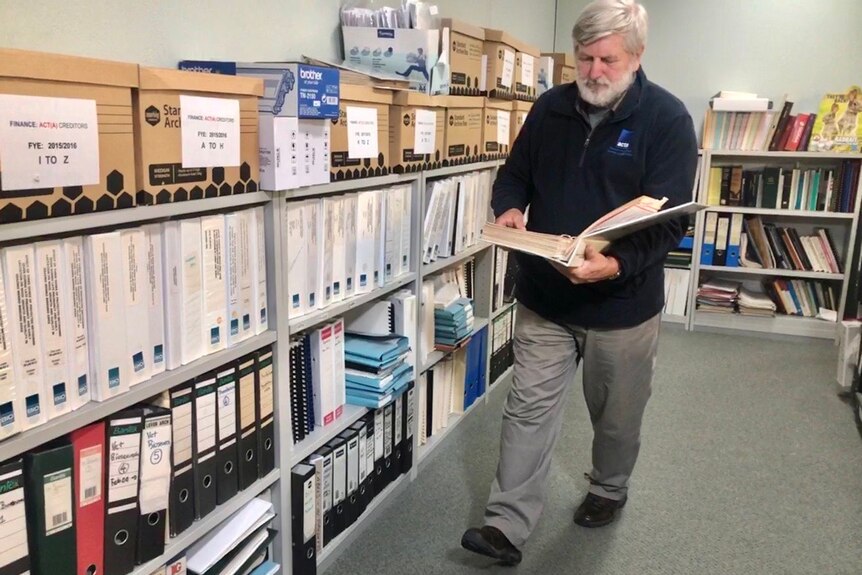 A man walking in his office past bookshelves full of paperwork