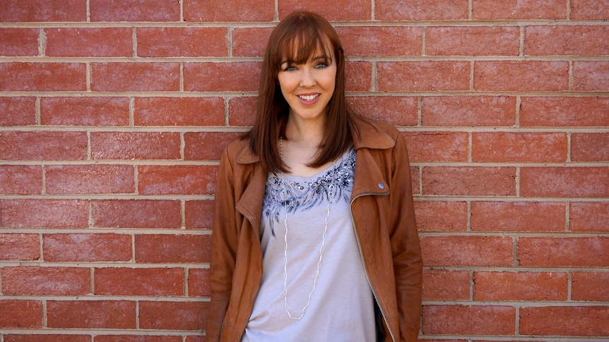 Rebekah Campbell is smiling, standing in front of a brick wall