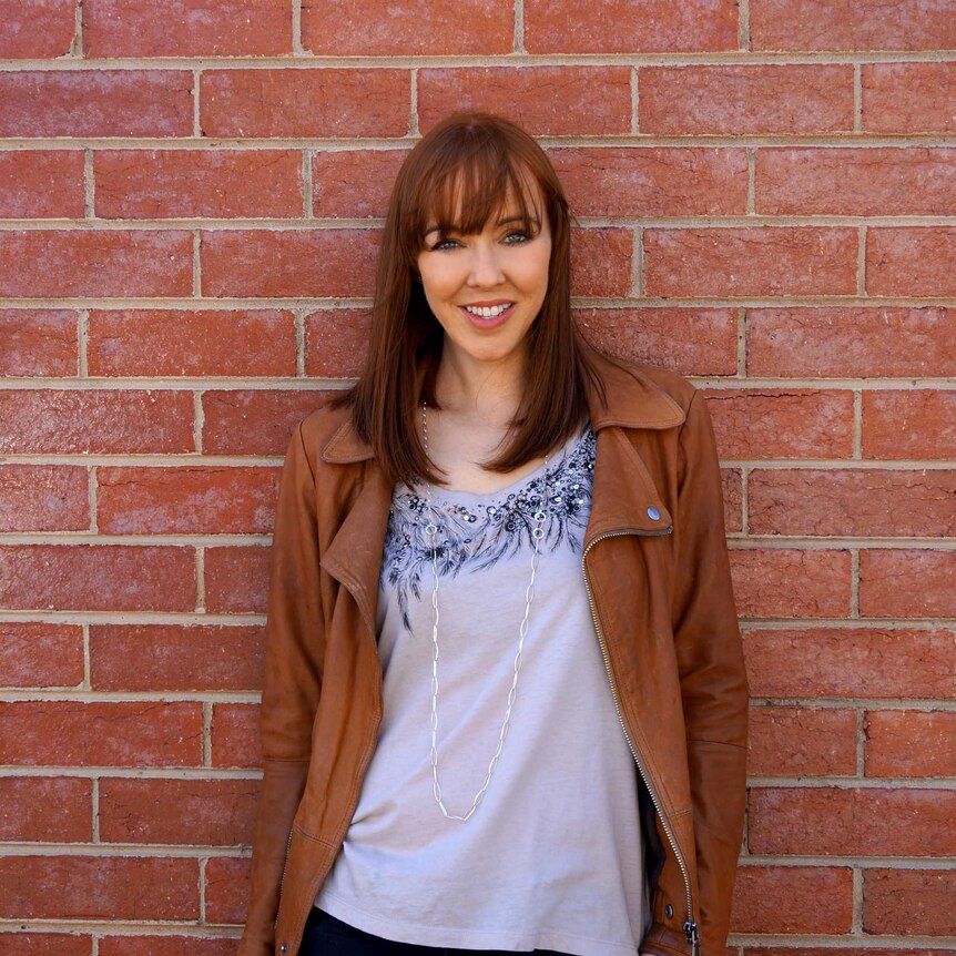 Rebekah Campbell is smiling, standing in front of a brick wall
