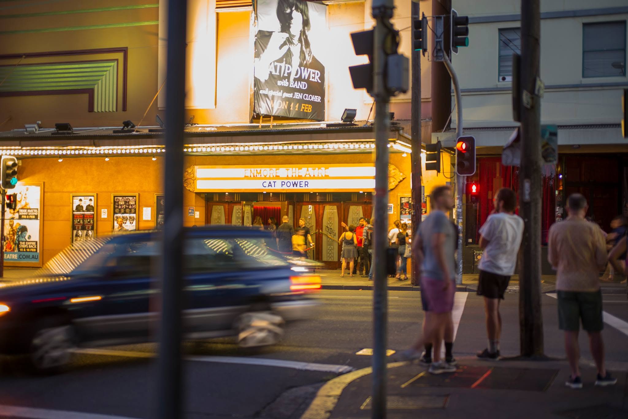 people stand at traffic lights opposite the enmore theatre in sydney